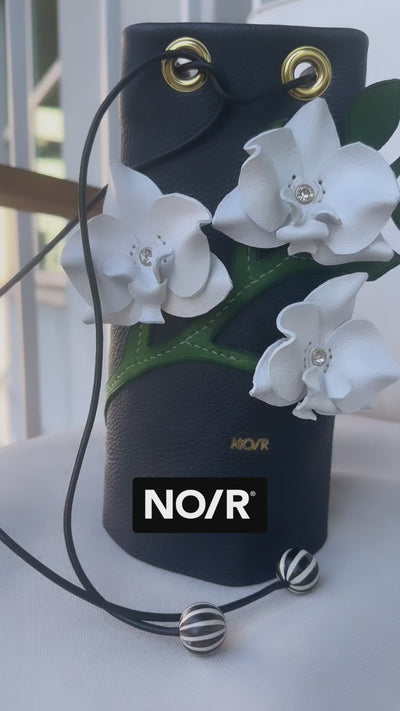 Norehearsal orchid bag vegtan leather hand painted bag, leaves and flowers sitting on white chair . work in progress.